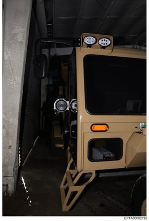 This photograph shows a tan or beige-colored vehicle, possibly a Hummer or similar large SUV, parked in what appears to be an underground parking structure or covered garage. The vehicle is equipped with roof-mounted LED lighting fixtures and is posi
