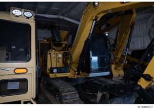 This photograph shows the interior cabin of a yellow Caterpillar (CAT) excavator or similar heavy construction equipment, displaying the operator's seating area, control systems, and instrumentation. The image appears to be documentation of equipment