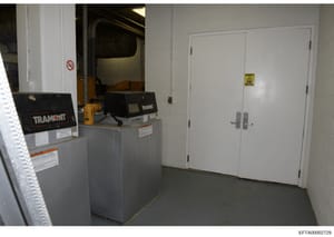 This is an evidence photograph showing an interior electrical/utility room containing TRANSNIT transformer equipment, safety signage, and industrial electrical infrastructure. The room appears to be part of a larger building's utility system and is d