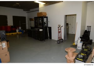 This is a photograph of an interior industrial or warehouse space showing various equipment, machinery, and storage items. The space appears to be under renovation or preparation, with exposed ceiling elements, cardboard boxes, industrial machinery (