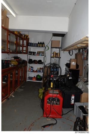 This photograph shows the interior of a storage or utility room, possibly at one of Epstein's properties. The space contains various equipment including a red industrial machine (possibly a dehumidifier or power tool), wooden cabinets with glass door