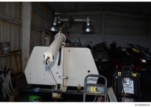 This photograph depicts the interior of an industrial warehouse or storage facility containing various equipment and machinery. The image shows a white industrial apparatus or tank suspended under overhead lighting, along with pressure washing equipm