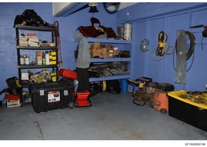 This is an evidence photograph showing the interior of a storage or utility room, likely from an Epstein property. The room contains various tools, equipment, supplies, and materials organized on shelves and stored on the floor, including power tools