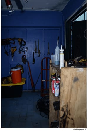 This photograph shows a blue-walled storage or utility room containing various maintenance and construction tools, equipment, and supplies. The image appears to be evidence documentation from a property investigation, showing organized tool storage o