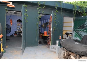 This is a photograph of the interior of a green-painted storage shed or container structure. The space contains various tools, equipment, and storage items including bicycles, shelving units, orange and red equipment (possibly recreational or mainten
