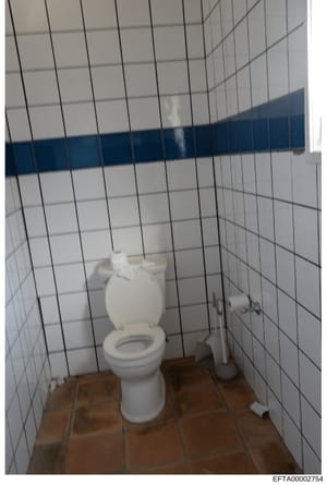 This is a photograph of a bathroom interior featuring white subway tile walls with a dark blue horizontal stripe, a white porcelain toilet, and terracotta tile flooring. The image appears to be evidence documentation from an Epstein-related property 