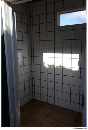 This is an evidence photograph showing the interior of a small room with white subway tile walls and a dark tile floor. The room appears to be a bathroom or utility space, photographed during daytime with natural light entering through a window. The 