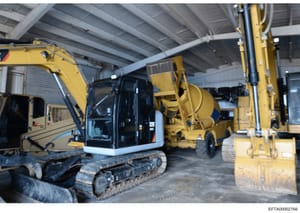 This photograph shows an industrial warehouse or equipment storage facility containing multiple pieces of heavy construction equipment, including excavators and a concrete mixer truck. The image documents equipment assets that may be relevant to prop