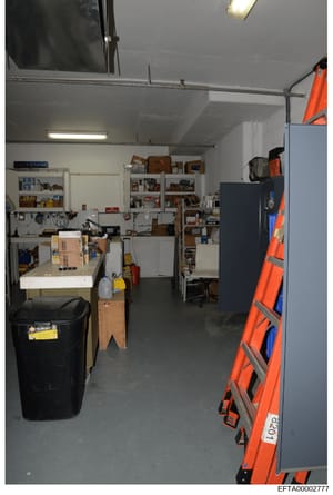 This is an evidence photograph showing the interior of a garage or workshop space containing various tools, equipment, and storage items. The space includes shelving units, a workbench, ladders, tool storage, and miscellaneous household/maintenance i