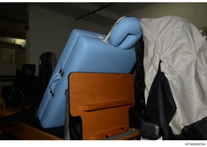 This is an evidence photograph from the Epstein investigation showing a blue inflatable item (possibly a massage table or similar object) and an orange/brown box in what appears to be an indoor storage or evidence facility. The items are partially co