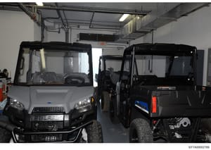 This photograph shows the interior of an industrial or commercial garage space containing three Polaris brand utility vehicles (ATVs/UTVs) in various states of assembly or storage. The image documents equipment found during the investigation, with ve