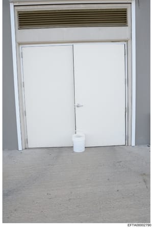 This is an evidence photograph showing the interior of a property, depicting a double white door with an overhead ventilation/air return system and a white bucket on the floor. The image appears to be part of property documentation or evidence collec