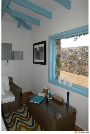 This photograph depicts an interior room, likely a bedroom or guest room, featuring modern design elements with turquoise architectural details and furnishings. The room has white walls, exposed turquoise ceiling beams, wicker furniture, and a large 