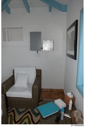 This is an evidence photograph showing a bedroom interior with simple furnishings and coastal-themed décor, including turquoise ceiling beams, wicker furniture, and minimal personal items. The photo appears to be documentation of a residential space,