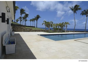 This photograph shows the exterior of a luxury oceanfront property featuring a swimming pool, expansive patio deck, manicured grounds with palm trees, and ocean views. The image appears to be documentation of a residential property likely owned or as