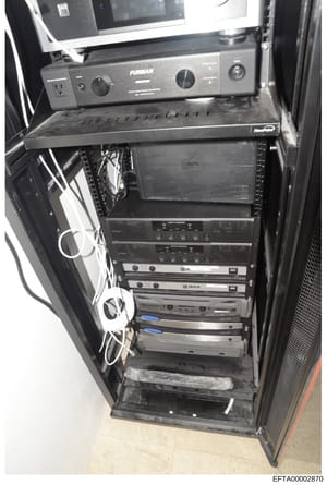 This photograph depicts a professional equipment rack containing audio amplifiers, APC power management systems, and related electronic components. The image shows the interior setup of technical infrastructure, with visible Furman power conditioner 