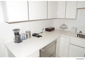 This photograph shows a modern kitchen interior with white cabinetry, white quartz countertops, and stainless steel appliances. The image appears to be documentation of a property interior, possibly from an Epstein residence. Various small appliances