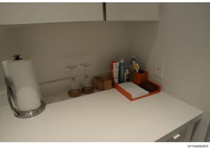 This is a photograph of a kitchen counter or shelf space showing various household items including a paper towel holder, glassware, decorative containers, and personal care products. The image appears to be an evidence photo from a property search or