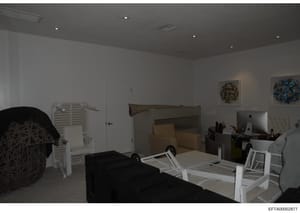 This is a photograph of an interior room, likely a bedroom or office space, showing various furniture items including a bed frame, desk with computer equipment, white storage units, and decorative wall art. The image appears to be evidence documentat