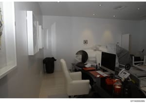 This is an evidence photograph showing the interior of a bedroom that appears to serve dual purposes as both a sleeping and working space. The room contains a bed, computer workstation, office furniture, and what appears to be medical or monitoring e