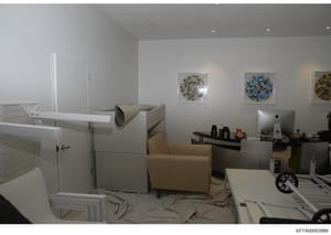 This photograph depicts an interior room with modern furnishings and decor, including a tan/beige armchair, white cabinetry, a desk setup with computer monitor, and wall art featuring circular blue and yellow designs. The room appears to be a residen