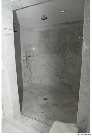 This is a photograph of a modern, upscale bathroom shower enclosure with marble tile walls and floor. The image appears to be an evidence or property documentation photo taken as part of the investigation, showing the interior finishes and fixtures o
