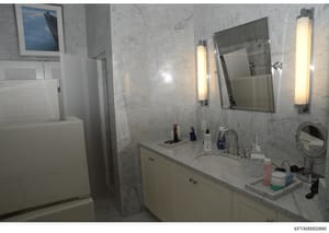 This is an evidence photo of a luxury bathroom featuring marble walls and countertops, double vanity sink, mirrored medicine cabinet, and contemporary lighting fixtures. The image appears to be from an Epstein property documentation effort, likely us