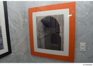 This is a photograph of a modern bathroom interior, showing marble tile walls, a recessed medicine cabinet with an orange frame and white border containing a mirror, and a light switch. The image appears to be evidence documentation from a property i