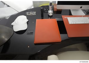This is an evidence photograph showing a luxurious office desk setup featuring a black desktop with orange/coral Hermes leather accessories, including what appears to be a portfolio or document holder. The desk contains personal items including an Ap