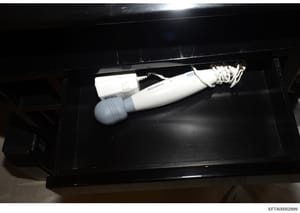 This is an evidence photograph showing a white handheld massager device with a power cord, photographed inside a black plastic evidence container. The photo was taken as part of the Epstein investigation documentation and is catalogued with the evide