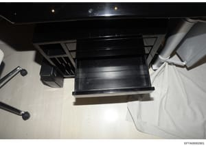 This is an overhead photograph showing a black furniture item, possibly a desk, shelf unit, or cabinet, positioned in an interior room with light-colored flooring and white walls. The image appears to be evidence documentation from a property search 