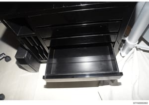 This photograph shows a black cabinet or storage unit with an open drawer, taken from above at an angle. The image appears to be evidence documentation from the investigation, showing the interior of what may be a desk, filing cabinet, or similar fur