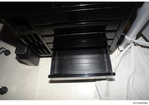 This is an evidence photograph showing a black wooden furniture item, likely a desk or cabinet, with an open drawer. The image appears to be taken from above at an angle, showing the interior construction and hardware. The photograph includes visible