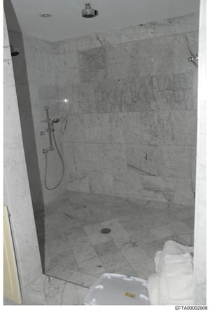 This is an evidence photograph documenting the interior of a luxury bathroom featuring marble tile walls and flooring, a walk-in shower with glass enclosure, and modern fixtures. The image appears to be part of property documentation or evidence coll