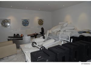This photograph shows an interior room equipped with massage tables, white pillows, professional spa/massage equipment, and decorative wall art. The space appears to be a massage or wellness facility with multiple treatment stations, storage areas, a