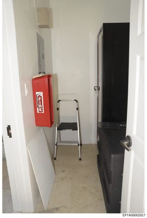 This is a photograph of a narrow interior hallway or utility space, likely within an Epstein property. The image shows standard building infrastructure including a red fire extinguisher, electrical panels, a step ladder, and what appears to be a blac