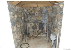 This photograph shows the interior of a stone-walled structure, likely a utility room, storage area, or building foundation space. The image documents electrical wiring, equipment mounting systems, and building infrastructure. The stone construction 