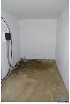 This photograph shows an interior view of an unfinished basement or cellar space with freshly painted white drywall, concrete flooring, and exposed electrical wiring and fixtures. The room appears to be under construction or renovation. The image is 