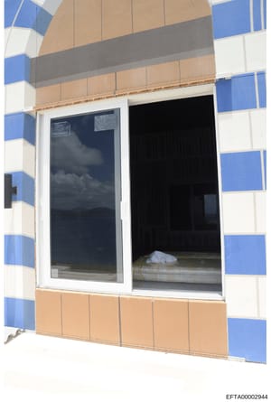 This is a photograph showing the interior view of a bedroom space accessed through a glass sliding door. The image captures the interior of what appears to be a residential unit with a distinctive blue and white striped exterior wall pattern visible 