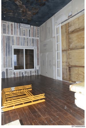 This photograph shows an interior room in mid-renovation or construction, featuring exposed elements, building materials, and temporary coverings. The space displays a dark hardwood floor, wallpaper samples or protective coverings on walls, wooden pl