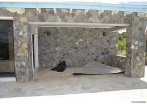 This is a photograph of an interior room during construction, featuring distinctive stone walls with mixed gray and tan aggregate patterns. The space appears to be a residential or commercial property undergoing renovation, with a concrete floor, whi