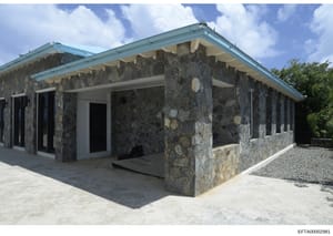 This photograph shows the exterior of a contemporary residential building featuring distinctive dark stone walls with light-colored accents, turquoise metal roofing, and modern architectural design. The structure appears to be a property potentially 