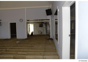 This photograph shows an interior room or commercial space that appears to be undergoing renovation or construction. The space features light blue/lavender walls, wooden flooring, multiple doorways, exposed electrical wiring, and construction equipme