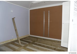 This is a photograph of an interior room in the process of renovation or construction. The image shows exposed framing, drywall in various stages of installation, and preparation work. The room features a lavender-painted wall on the left, a brown co