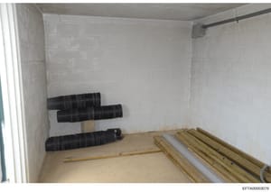 This photograph shows an unfinished interior room or storage space with drywall, containing black corrugated piping and wooden construction materials. The image appears to be documentation of property conditions or construction materials relevant to 