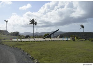 This photograph shows an expansive landscaped property with tropical vegetation, manicured lawns, and a distinctive modern art installation or architectural feature in the center. The image appears to be documentation of real estate or property groun