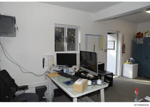 This is a photograph of a modern office or administrative workspace containing two computer monitors, desk equipment, and storage. The clean, minimalist white walls and organized layout suggest this may be an office used by Epstein's organization or 