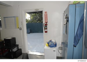This is an evidence photograph showing the interior of a residential property, likely part of a location searched during the Epstein investigation. The image captures a doorway leading to an outdoor area, with visible fire safety equipment mounted on