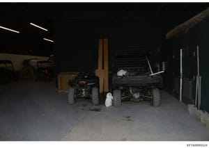 This photograph shows the interior of a large storage facility or garage containing multiple all-terrain vehicles (ATVs), a forklift, and various equipment and supplies. The image appears to be evidence documentation, likely taken during a property s