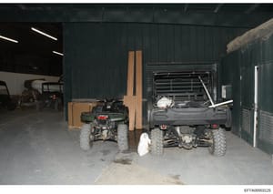 This is a photograph showing the interior of a metal-clad warehouse or storage facility containing multiple all-terrain vehicles (ATVs), including green and black Kawasaki models, along with various tools and equipment. The image appears to be eviden